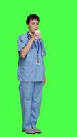 Side view Medical assistant drinking cup of coffee before starting exam appointments in the morning, enjoying caffeine refreshment against greenscreen backdrop. Nurse drinks beverage. Camera A. video