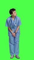 Front view Medical assistant being impatient against greenscreen backdrop, looking around and waiting for patients at consultations. Nurse with health expertise feeling frustrated while she waits. Camera A. video