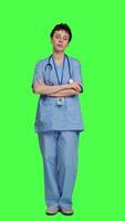 Front view Portrait of confident medical assistant posing with arms crossed in studio, standing against greenscreen backdrop. Successful nurse with healthcare expertise wearing blue scrubs uniform. Camera A. video