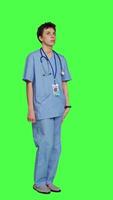 Side view Stressed nurse checking time on watch and waiting for patient to arrive at checkup examination, being impatient against greenscreen backdrop. Medical assistant with scrubs and stethoscope. Camera A. video