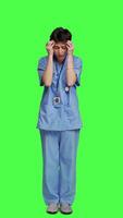 Front view Stressed furious nurse screaming at someone against greenscreen backdrop, showing rage and anger in studio. Aggressive upset medical assistant shouting and being dissatisfied. Camera A. video