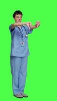 Side view Displeased medical assistant shows thumbs down in studio, presenting her disapproval and disagreement with dislike symbol against greenscreen. Nurse feeling unhappy with rejection sign. Camera A. video