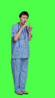 Side view Medical assistant asking to keep quiet and be silent against greenscreen, showing hush mute symbol to keep privacy and silence. Young nurse showing secrecy taboo sign. Camera A. video