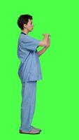 Profile Medical assistant giving timeout symbol against greenscreen backdrop, showing limits and asking for a break. Nurse doing pause or stop gesture while she wears blue scrubs. Camera A. video