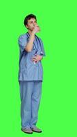Side view Healthcare specialist enjoying hot coffee cup against greenscreen backdrop, drinking caffeine refreshment in blue scrubs. Medical assistant serving beverage at work, friendly staff. Camera A. video