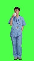 Front view Medical assistant drinking cup of coffee before starting exam appointments in the morning, enjoying caffeine refreshment against greenscreen backdrop. Nurse drinks beverage. Camera A. video