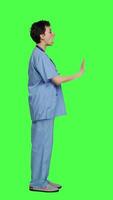 Profile Health specialist with blue scrubs showing stop sign in studio, standing against greenscreen backdrop. Nurse expressing denial and refusal with warning forbidden symbol, denying something. Camera A. video