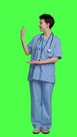 Front view Healthcare specialist presenting a thing for promotional ad in studio, pointing at something against greenscreen backdrop. Medical assistant creating a web commercial, health expertise. Camera A. video