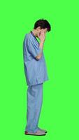 Profile Unwell nurse suffering from a headache against greenscreen backdrop, wearing scrubs and feeling overworked at hospital. Medical assistant having a painful migraine, stress and burnout. Camera A. video