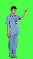 Side view Woman nurse waving hello and inviting people to come closer, calling over patients for checkup examinations against greenscreen. Medical assistant greeting persons and asking them to come. Camera A. video