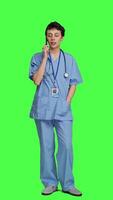 Front view Health specialist using smartphone to make important calls, standing against greenscreen backdrop. Nurse talking to patients for checkup exams on telephone line, calling people to confirm. Camera A. video