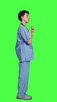 Profile Smiling medical assistant applauding someone in studio, celebrating success and cheering against greenscreen backdrop. Young nurse clapping hands and feeling happy about achievement. Camera A. video