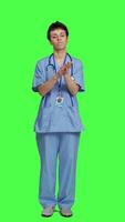 Front view Smiling medical assistant applauding someone in studio, celebrating success and cheering against greenscreen backdrop. Young nurse clapping hands and feeling happy about achievement. Camera A. video