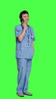 Side view Health specialist using smartphone to make important calls, standing against greenscreen backdrop. Nurse talking to patients for checkup exams on telephone line, calling people to confirm. Camera A. video