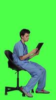 Profile Medical assistant browsing internet on tablet while she sits down in a chair, killing time by scrolling on social media apps and texting friends. Nurse in scrubs using modern gadget. Camera A. video