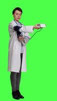 Side view Healthcare specialist using a tonometer to measure high blood pressure and pulse, presenting tool used at checkup examinations. Doctor in white coat stands against greenscreen backdrop. Camera A. video