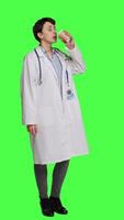Side view Happy medic serving hot coffee cup as refreshment against greenscreen backdrop, wearing white coat and drinking caffeine beverage. General practitioner enjoying drink, medical expertise. Camera A. video