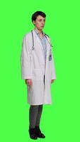 Side view Physician saying no and showing negative reaction symbol in studio, wearing a white coat and standing against greenscreen backdrop. Woman medic feeling displeased, rejection sign. Camera A. video