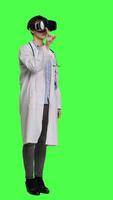 Side view Physician consulting patients with virtual reality futuristic glasses, wears white coat against greenscreen backdrop. General practitioner uses artificial intelligence interactive headset. Camera A. video