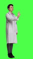Side view Woman physician raising palm and doing stop sign in studio, expressing rejection and denial against greenscreen backdrop. General practitioner showing warning symbol with negative reaction. Camera A. video