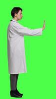 Profile Woman physician raising palm and doing stop sign in studio, expressing rejection and denial against greenscreen backdrop. General practitioner showing warning symbol with negative reaction. Camera A. video