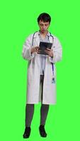 Front view General practitioner studying radiography scan results for patients with disease, stands against greenscreen backdrop. Medic examines x ray diagnosis, works with a tablet. Camera A. video