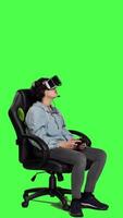 Side view Woman playing video games on console with controller and vr headset, sitting against greenscreen backdrop. Gamer having fun with online tournament, virtual reality interactive cyberspace. Camera A.