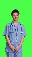 Front view Portrait of medical assistant smiling and posing with confidence, standing against greenscreen backdrop. Nurse wears blue scrubs and stethoscope, feeling successful with health expertise. Camera B. video