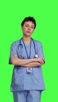 Front view Portrait of confident medical assistant posing with arms crossed in studio, standing against greenscreen backdrop. Successful nurse with healthcare expertise wearing blue scrubs uniform. Camera B. video