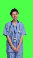 Front view Cheerful smiling medical assistant standing against greenscreen backdrop, feeling confident and successful while she wears hospital scrubs. Nurse surgeon works in healthcare industry. Camera B. video