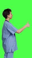 Profile Cheerful nurse giving thumbs up sign against greenscreen backdrop, showing positive gesture with a like. Medical assistant shows her approval, recommending something and being satisfied. Camera B. video