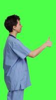 Profile Cheerful nurse giving thumbs up sign against greenscreen backdrop, showing positive gesture with a like. Medical assistant shows her approval, recommending something and being satisfied. Camera B. video