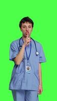 Front view Medical assistant asking to keep quiet and be silent against greenscreen, showing hush mute symbol to keep privacy and silence. Young nurse showing secrecy taboo sign. Camera B. video