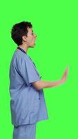 Profile Health specialist with blue scrubs showing stop sign in studio, standing against greenscreen backdrop. Nurse expressing denial and refusal with warning forbidden symbol, denying something. Camera B. video