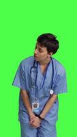 Front view Medical assistant being impatient against greenscreen backdrop, looking around and waiting for patients at consultations. Nurse with health expertise feeling frustrated while she waits. Camera B. video