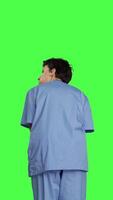 Back view Stressed nurse being in a hurry with the checkup appointments, waiting for patients to arrive at examinations. Medical assistant with scrubs acting impatient against greenscreen backdrop. Camera B. video