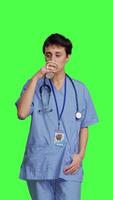 Front view Healthcare specialist enjoying hot coffee cup against greenscreen backdrop, drinking caffeine refreshment in blue scrubs. Medical assistant serving beverage at work, friendly staff. Camera B. video