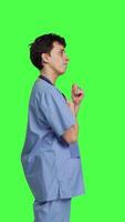 Profile Smiling medical assistant applauding someone in studio, celebrating success and cheering against greenscreen backdrop. Young nurse clapping hands and feeling happy about achievement. Camera B. video