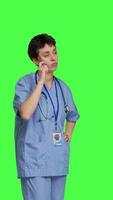 Side view Medical assistant thinking about new treatment ideas in studio, acting thoughtful while she stands against greenscreen backdrop. Pensive young nurse contemplating about healthcare ideas. Camera B. video