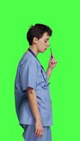 Profile Doubtful medical assistant thinking about ways to cure a disease in studio, stands against greenscreen backdrop and wearing scrubs. Nurse contemplating about new ideas, being pensive. Camera B. video