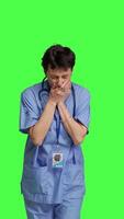 Front view Medical assistant feeling extremely sleepy against greenscreen backdrop, being overworked after the night shift. Woman nurse yawns and feels exhausted in studio, burnout and anxiety. Camera B. video