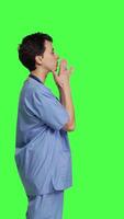 profil flörtig söt sjuksköterska blåser luft kyssar mot grönskärm bakgrund, varelse romantisk och uttrycker ljuv känslor. medicinsk assistent i scrubs håller på med härlig gest, uttrycker Sann kärlek. kamera b. video