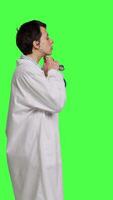 Profile General practitioner with a white coat using stethoscope in studio, preparing to examine patients at checkup appointments. Female doctor in uniform standing against greenscreen backdrop. Camera B. video