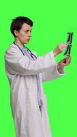 Seite Aussicht Frau Arzt untersucht x Strahl Scan zu finden Krankheit Diagnose zum geduldig, suchen beim Radiographie Ergebnisse zu bestimmen Krankheit und Heilung. Medizin Stehen gegen grüner Bildschirm Hintergrund. Kamera b. video
