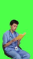 kant visie Gezondheid specialist is lezing een literatuur boek naar verkrijgen arts specialisatie en chirurg expertise, zittend in een stoel. verpleegster aan het studeren gezondheidszorg industrie lezing tegen groene scherm. camera b. video