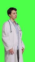 côté vue portrait de médecin portant une blanc manteau et une stéthoscope pour examens, permanent contre écran vert toile de fond. médecin spécialiste travail dans soins de santé industrie, médical compétence. caméra b. video