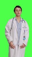 Front view Portrait of health specialist wearing a white hospital coat in studio, standing against greenscreen backdrop. Successful doctor posing with confidence, medical industry expertise. Camera B. video