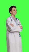 Side view Portrait of successful physician standing with arms crossed against greenscreen backdrop, wearing a white coat and stethoscope. Doctor feeling confident with healthcare expertise. Camera B. video