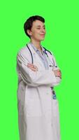 Side view Portrait of successful physician standing with arms crossed against greenscreen backdrop, wearing a white coat and stethoscope. Doctor feeling confident with healthcare expertise. Camera B. video