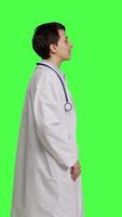 Profile Portrait of physician wearing a white coat and a stethoscope for exams, standing against greenscreen backdrop. Doctor specialist working in healthcare industry, medical expertise. Camera B. video